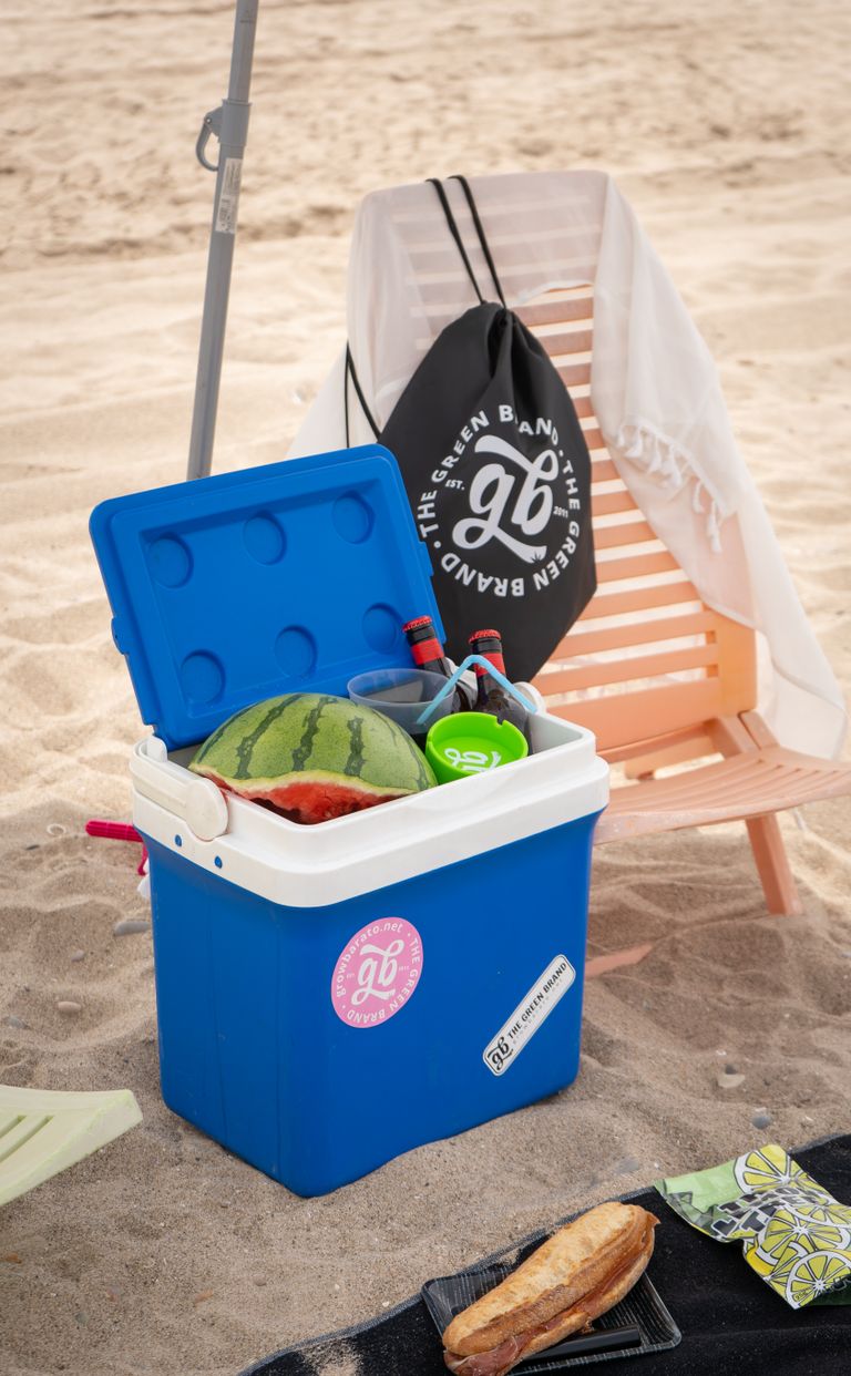 A vibrant beach setup with a cooler, watermelon, bag, and beach chair, perfect for a summer picnic day.