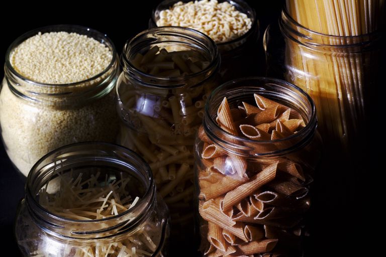 Different types of pastas and cereals in glass jars on kitchen in sunlight