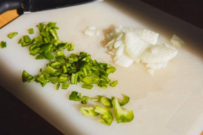Chopped green pepper and onion beside a knife on a cutting board