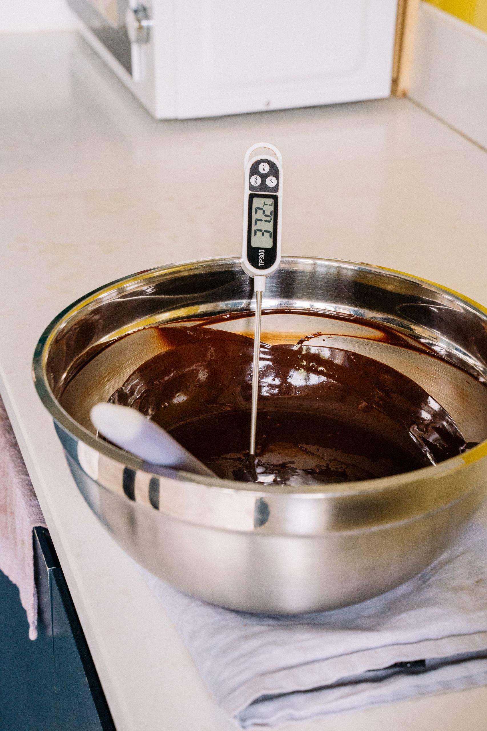 Stainless steel bowl with melted chocolate and digital thermometer on a kitchen counter.