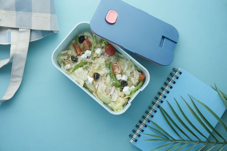 Top view of a nutritious salad lunch box with a notebook on a blue background.