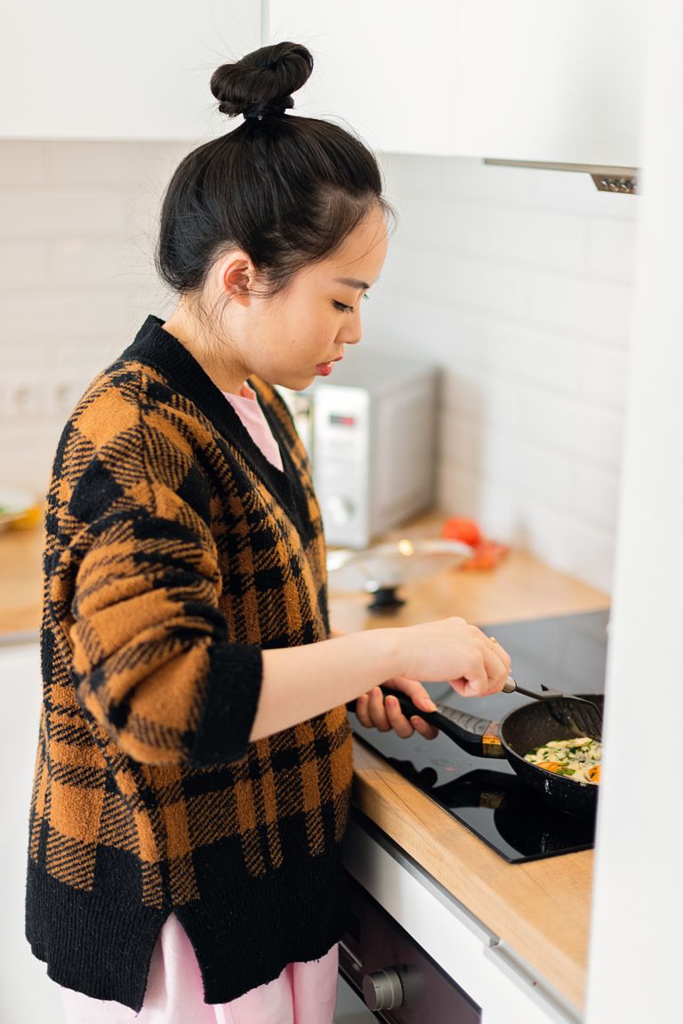 Young woman cooking a meal on the stove in a cozy kitchen setting.